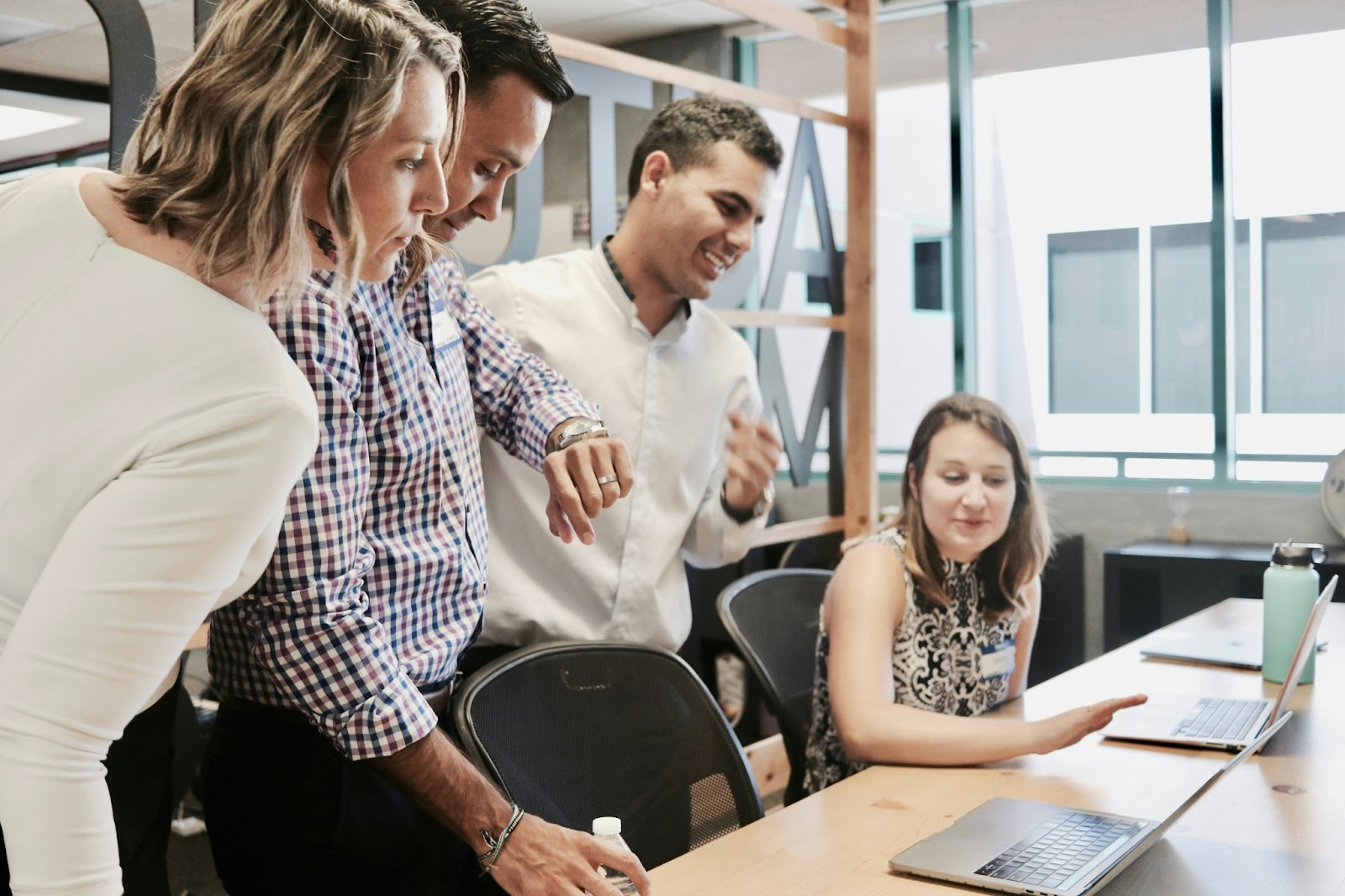 A woman sitting at a table while other three people, two men and a woman are looking at her laptop. They seem to be reviewing something.