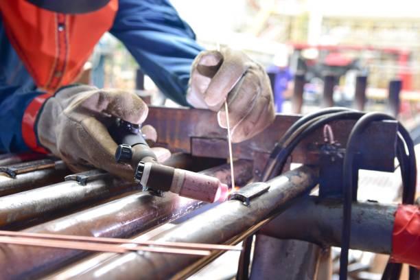 The welder is welding the plate to the pipe The welder is welding the plate to the pipe with Tungsten Inert Gas Welding process (TIG). The welder wears protective equipment with a mask and heat resistant gloves tig welding pipe stock pictures, royalty-free photos & images