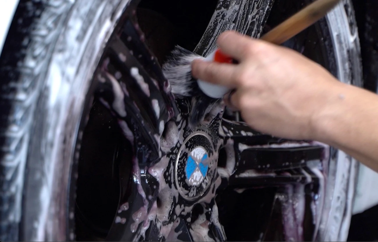 Expert pre-coating preparation, with a hand meticulously scrubbing a car wheel using a specialized brush, ensuring a clean surface for ceramic coating application.