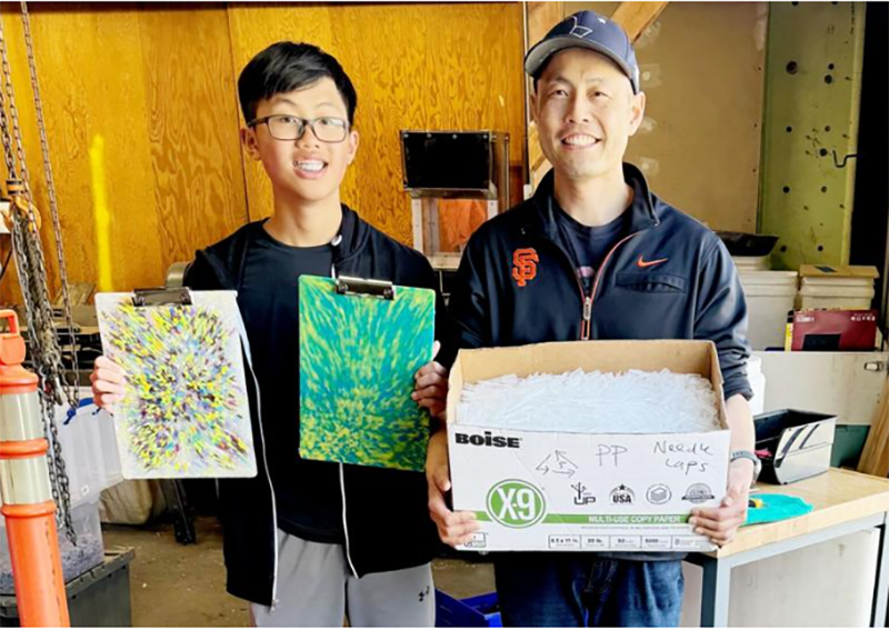 Brandon and his father with a box of clean syringe needle caps and clip boards they are repurposed into