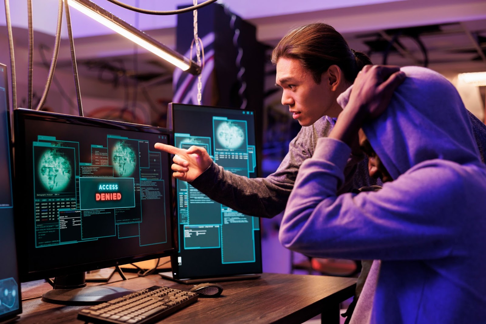 Two cybersecurity experts analyze computer screens showing “Access Denied” messages, indicating a security breach attempt