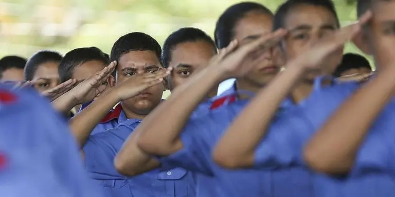 Jovens em colégio militares com fardas azuis batem continência 