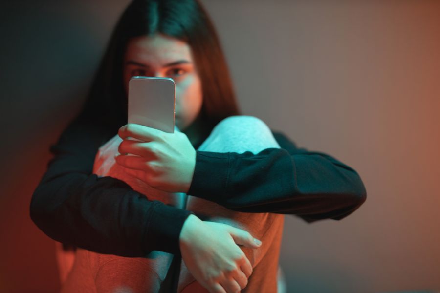 Girl sitting alone in the dark, looking at her phone screen.