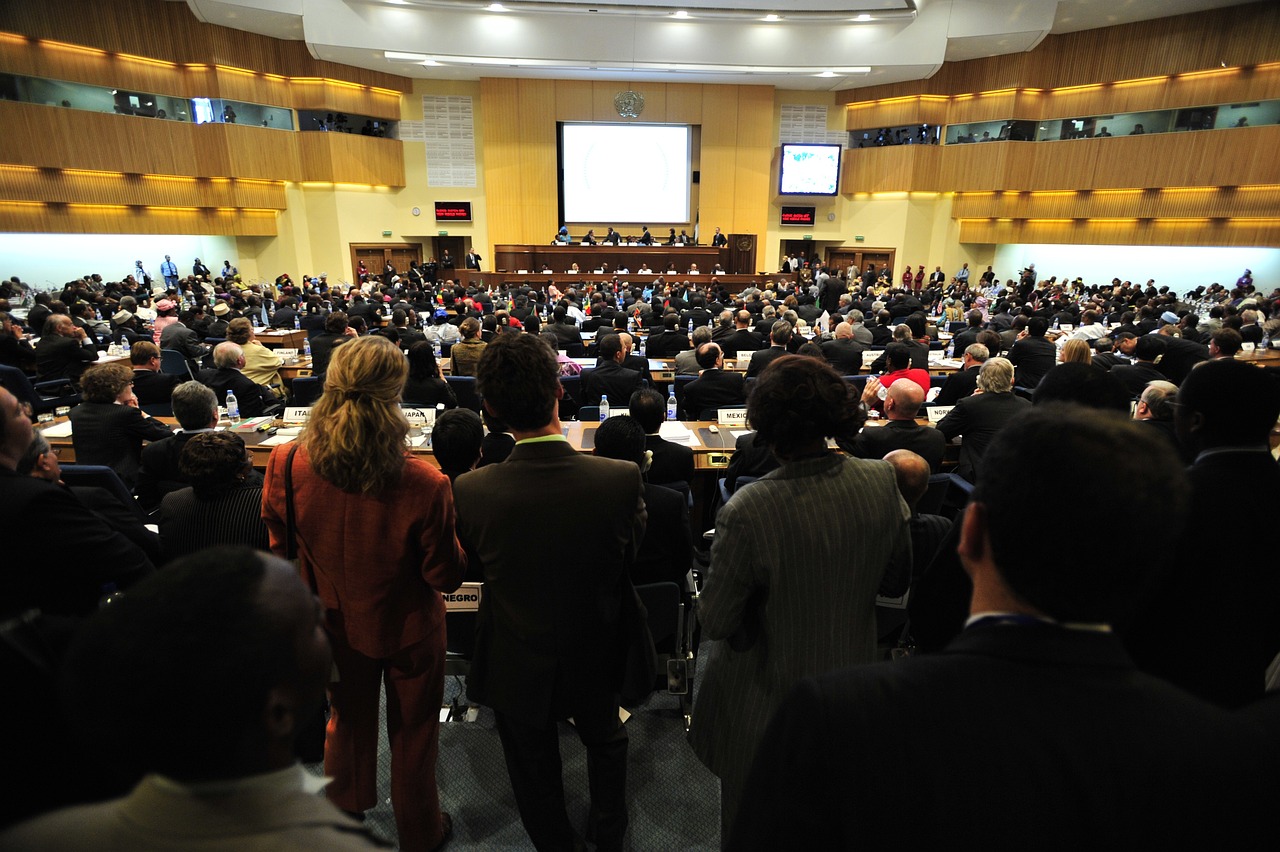 A large conference hall filled with people attending a conference, with speakers on a stage at the front and attendees seated in rows.