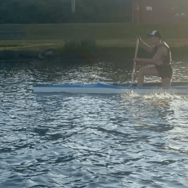 Tarzan glides gracefully through the water like she was born in a boat, riding a long and narrow sprint canoe or "C1" with just enough room to kneel on one knee (like a marriage proposal, which is just how much Tarzan loves her boat!). She wears a baseball hat, life jacket and shorts, pulling a long wooden paddle through the water.