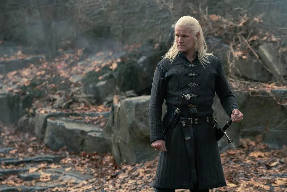 Daemon Targaryen (Matt Daemon) observa hacia un lado. Está a punto de empuñar su espada. El fondo se compone de hojas y árboles quemados en House of the Dragon temporada 2 x 6.