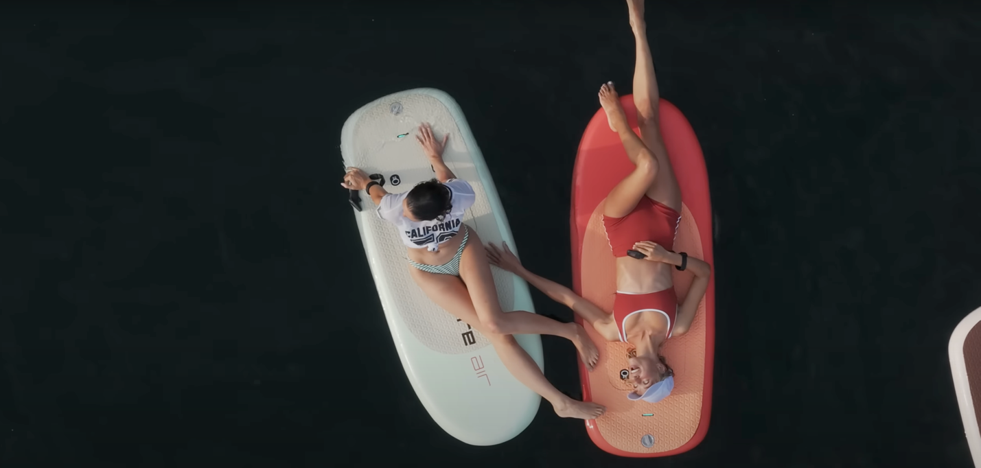 A person lying on a surfboard next to a person

Description automatically generated