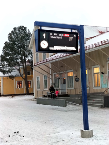 The sign indicating the final stop of the long train journey to Rovaniemi. In the background the Rovaniemi train station and two people exiting.