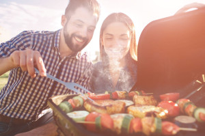 Friends making barbecue and having lunch in the nature. Couple having fun while eating and drinking at a pic-nic - Happy people at bbq party.