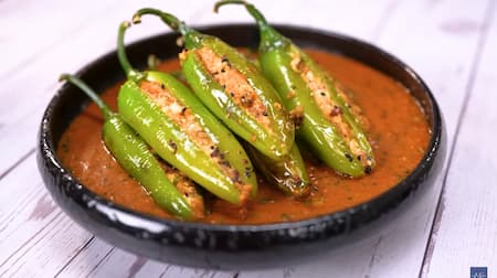 Stuffed green chilies arranged on a plate with thick, spicy gravy, garnished with fresh coriander leaves.