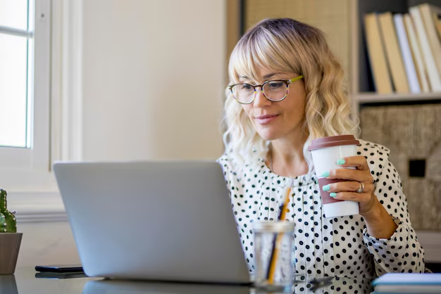 A female blogger sitting in front of a laptop with a coffee cup in hand