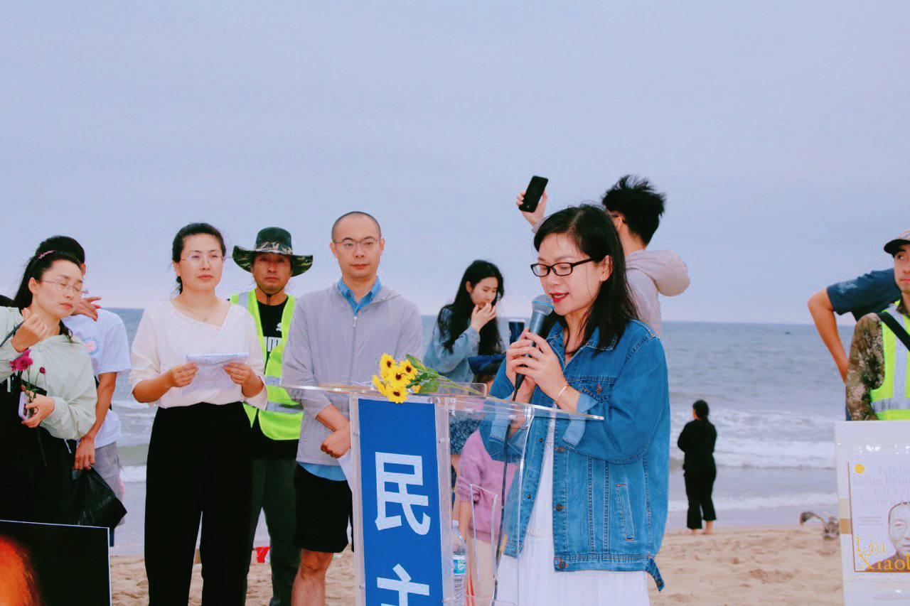 A person speaking at a podium on a beach
Description automatically generated