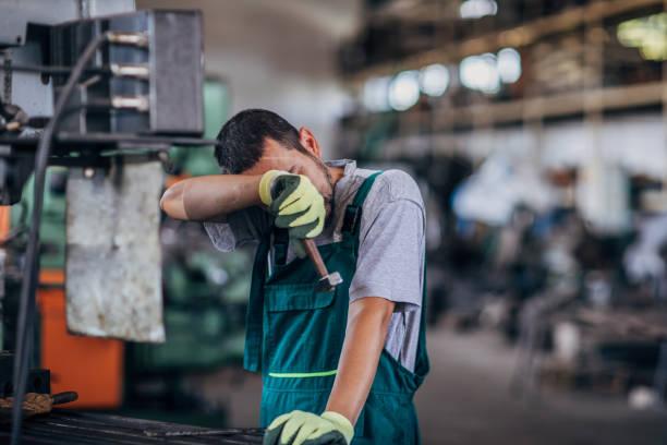Tired guy working on a machine in factory workshop One man, young man working on a machine in factory workshop alone. tired factory worker stock pictures, royalty-free photos & images