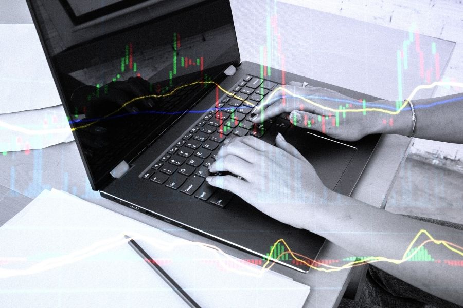 Hands typing on a laptop with financial graph overlay.