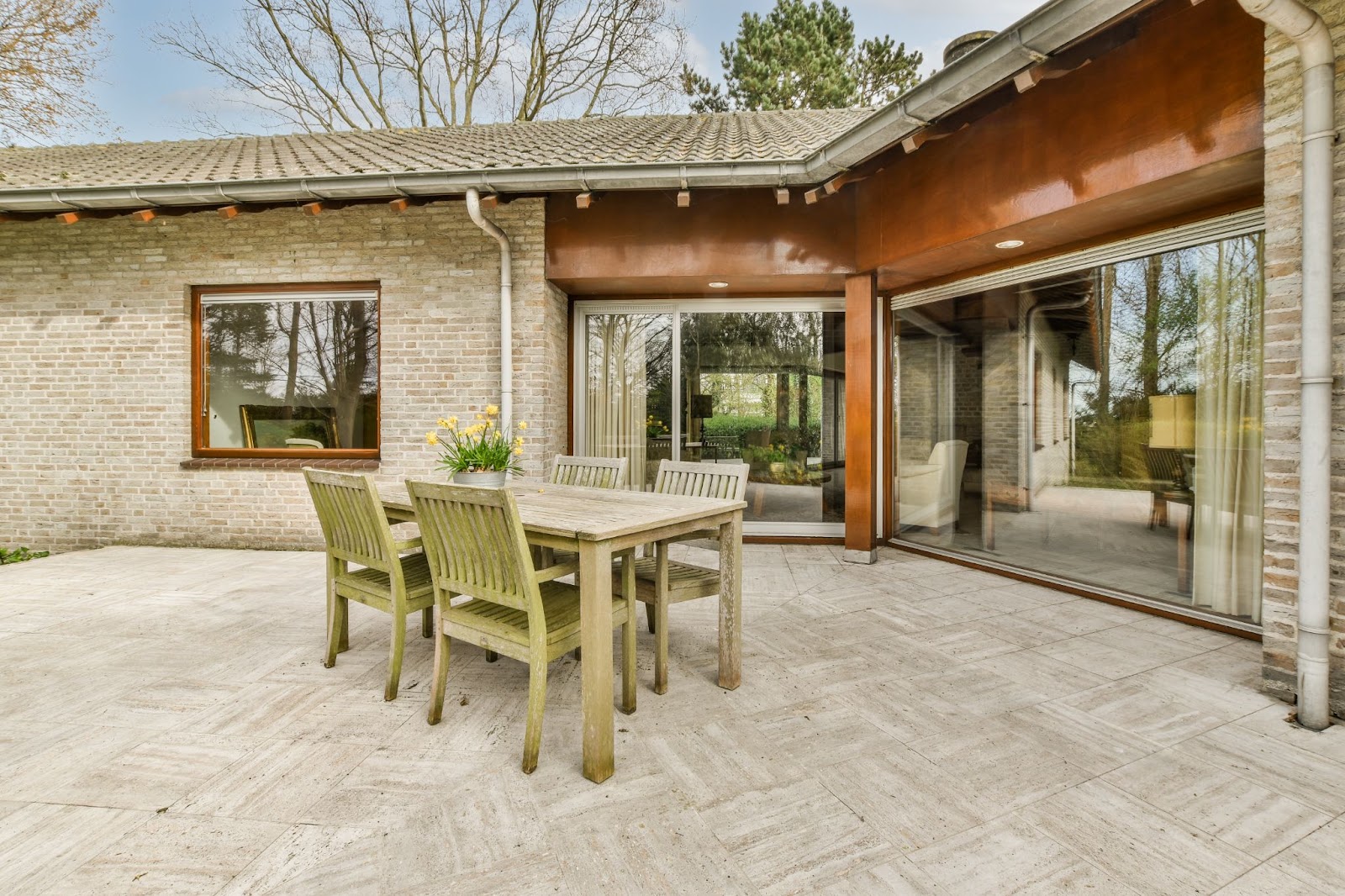 A neatly paved concrete patio featuring a cozy sitting area that complements the glass sliding doors and windows, set against light-colored brick walls for a harmonious outdoor ambiance.