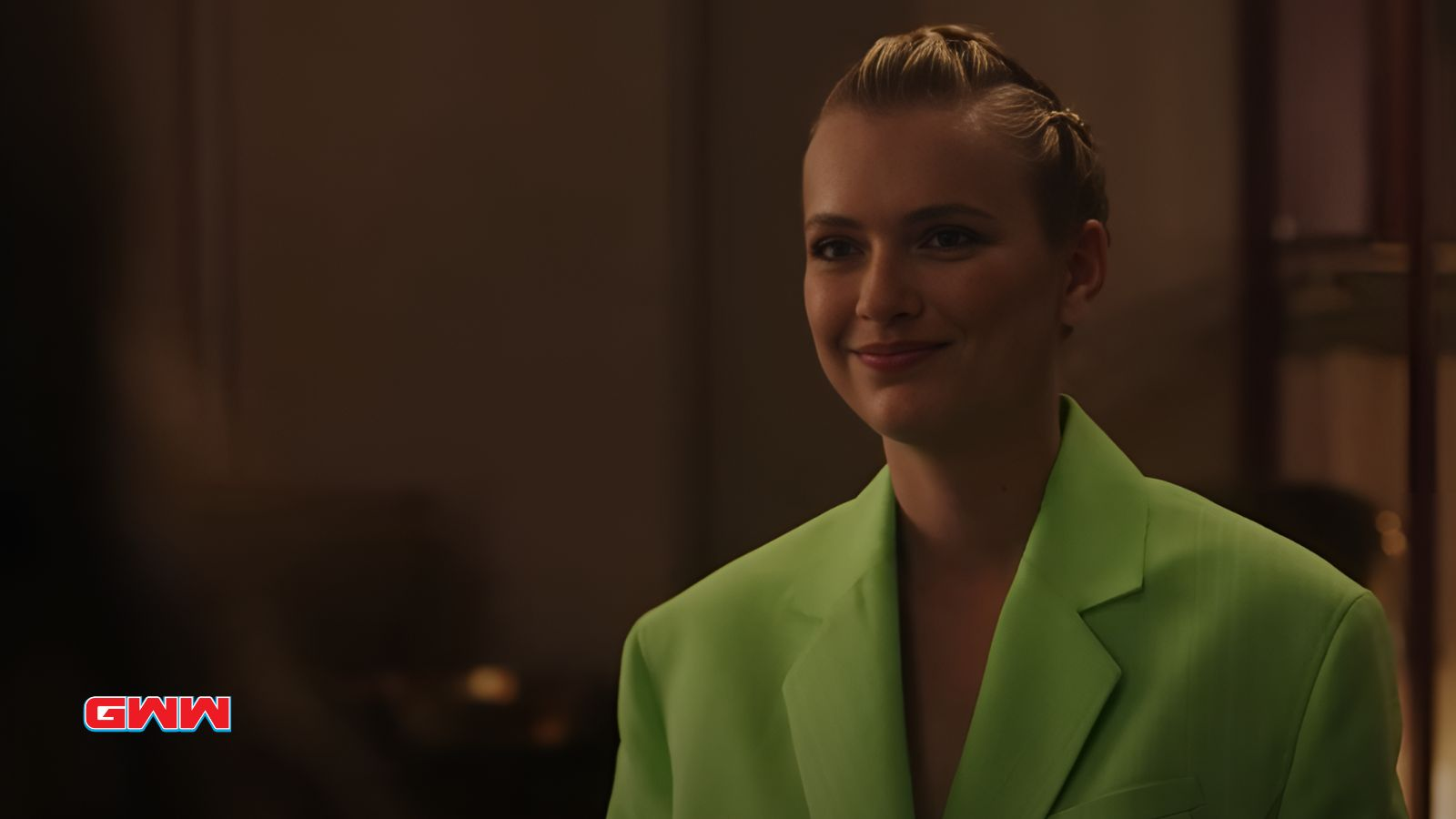 Camille in a bright green blazer smiling softly in a dimly lit room.