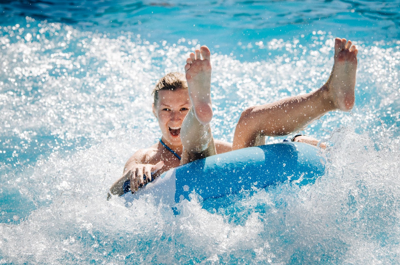 A mulher dá risada enquanto se equilibra sentada na boia caindo na piscina.