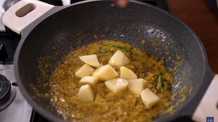 Diced potatoes being added to the cooked onion paste, ready to be sautéed.