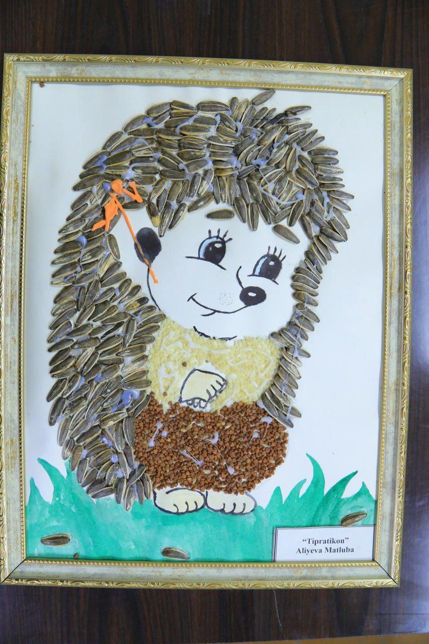 Cartoon figure of a small animal with wide-open eyes and a little black nose. Its body and hair is made of sunflower and other seeds. 