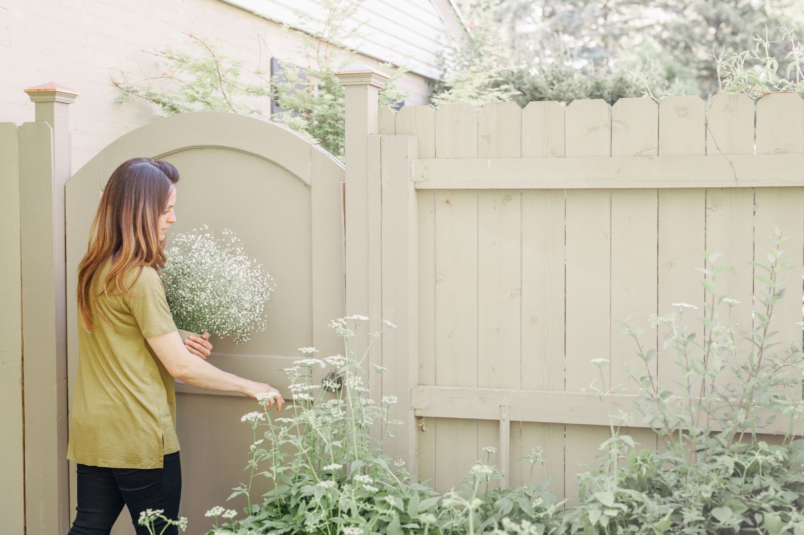  A woman in khaki shirt and black pants steps inside through a vinyl gate, clutching a bouquet of white flowers freshly picked from the lush rows of plants before her.