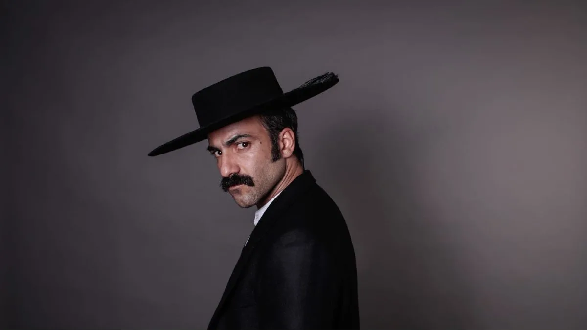 Gabriel Cañas como José Luis Echeñique, vistiendo un sombrero negro y mirando hacia la cámara.