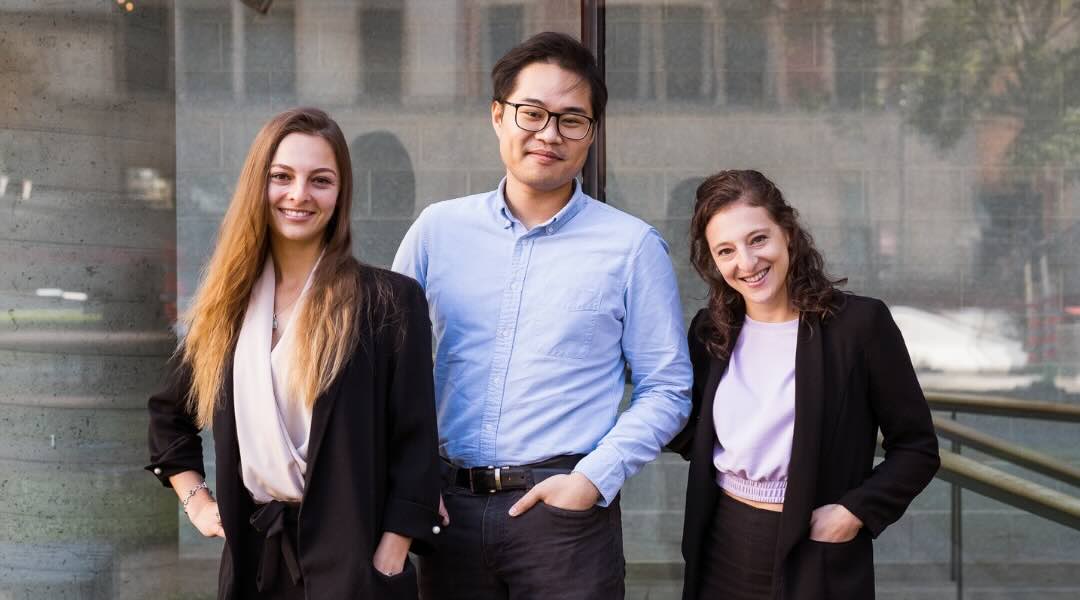 Three TeamNutrition dietitians nutritionists, two women and one man, standing together and smiling in front of a modern building.