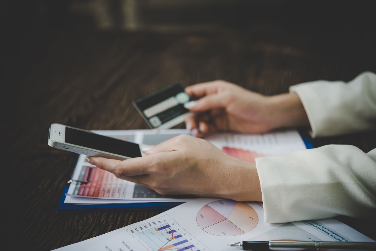 Person holding a credit card and a smartphone with financial documents on a desk