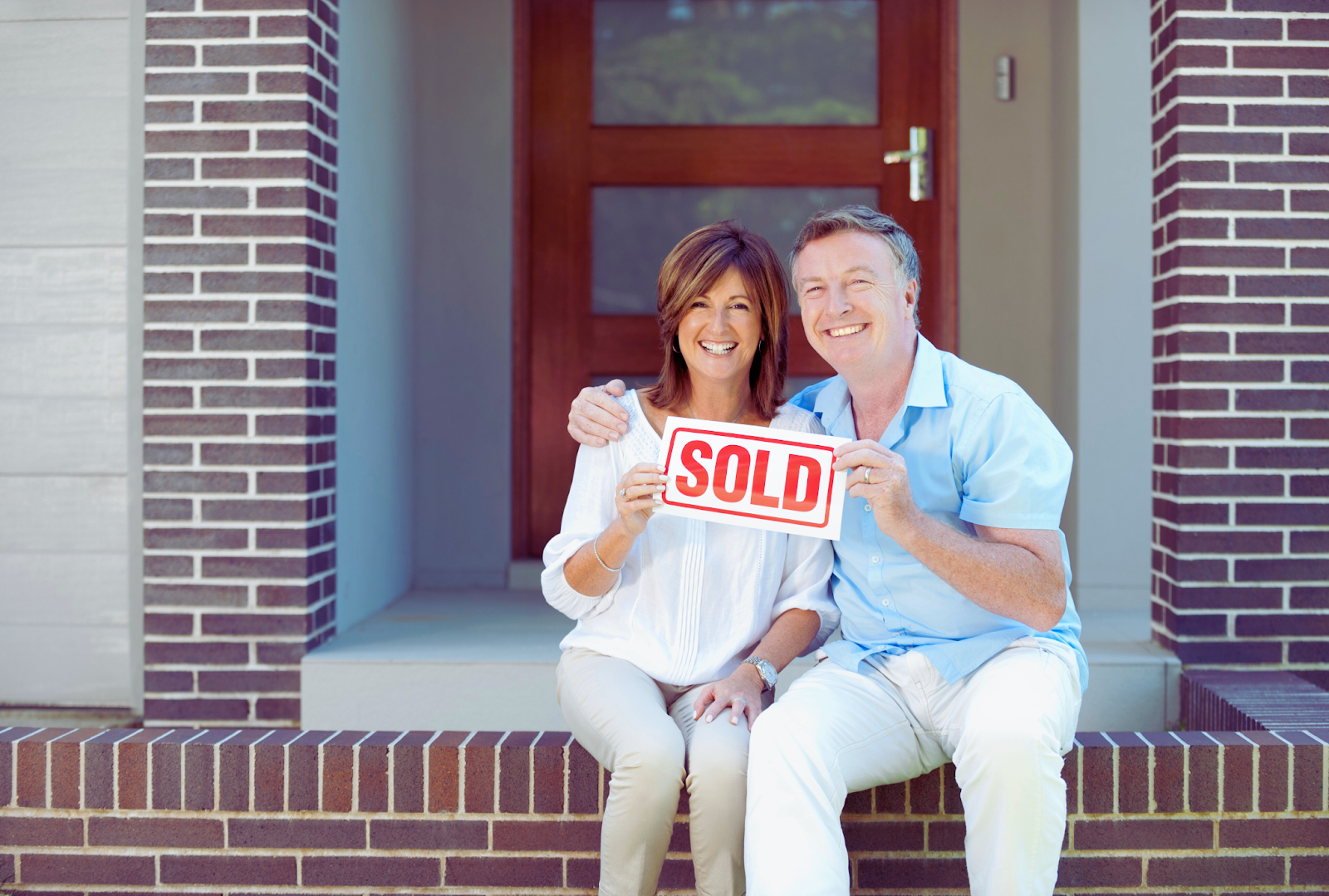 happy couple sitting in front of their recently sold home