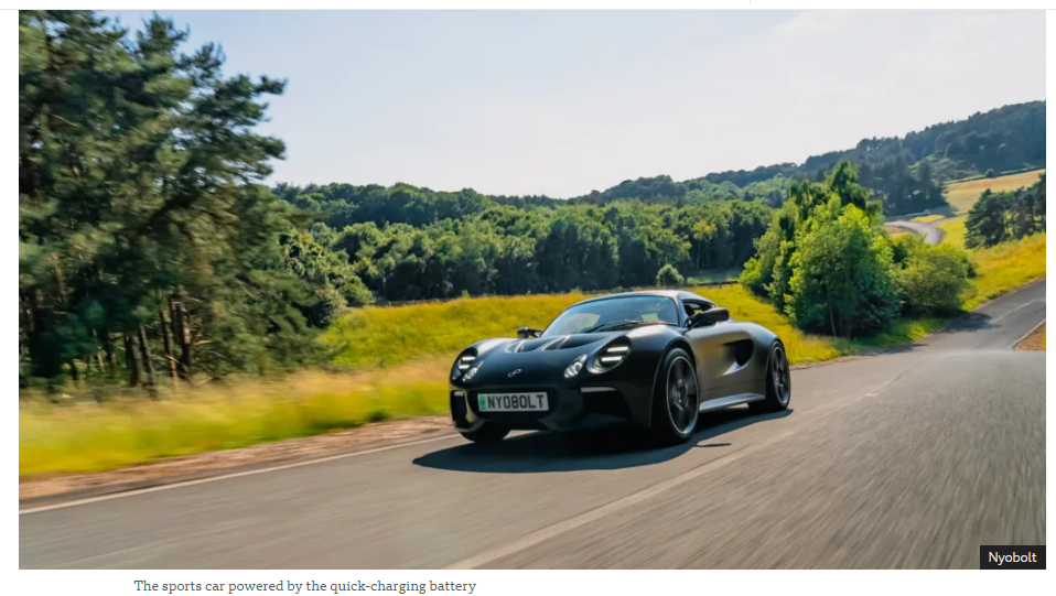 A black sports car on a road with trees in the background

Description automatically generated