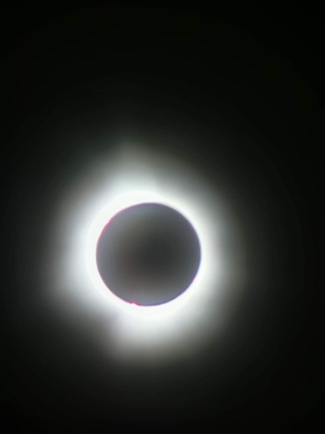 Total solar eclipse, very dark sky with the sun blocked showing its bright white corona around it.