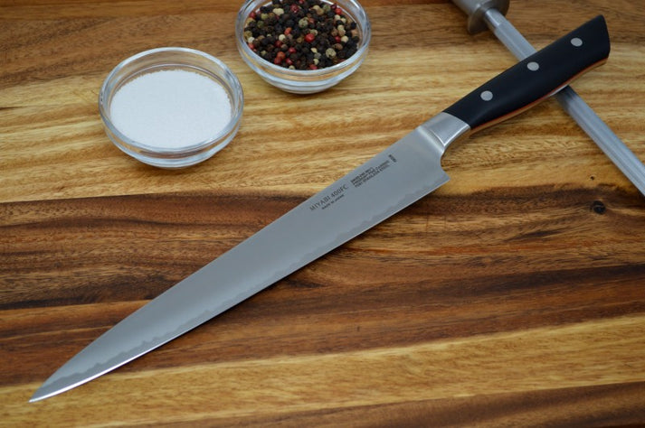 An image showing the Miyabi Evolution 9.5-inch slicing knife, with the handle resting on a sharpening rod. To the right of the knife are cups of salt and pepper.