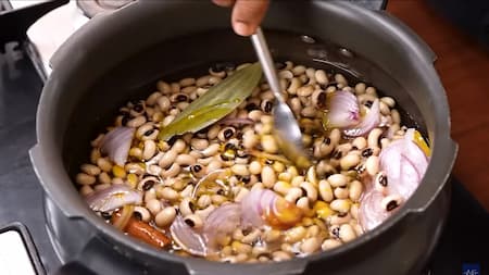 A pressure cooker filled with soaked lobia, sliced onions, and aromatic spices like black cardamom, cloves, and bay leaves, ready for cooking.