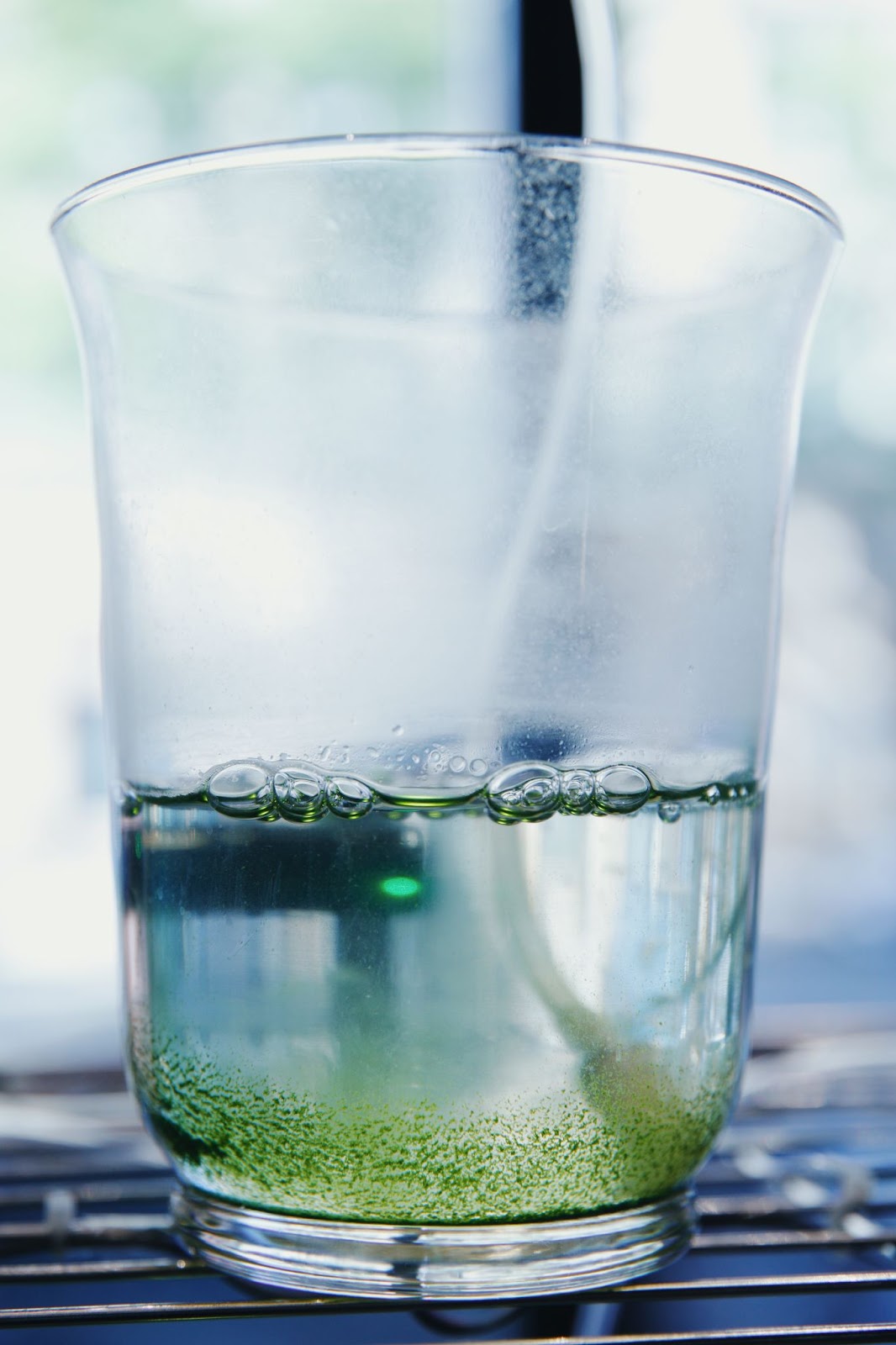 close image of a glass on a storage shelf. a liquid can be seen in the glass, with algae along the bottom.