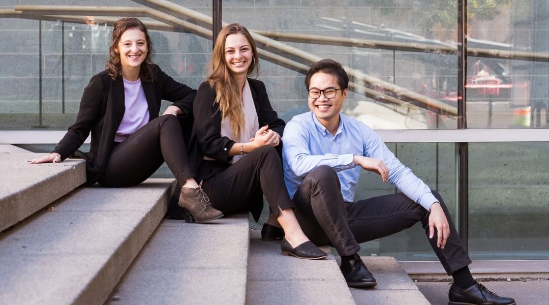 Trois jeunes nutritionniste diététistes d'ÉquipeNutrition, deux femmes et un homme, assis de manière décontractée sur des marches extérieures. Ils sont vêtus en tenue professionnelle décontractée et sourient à la caméra.