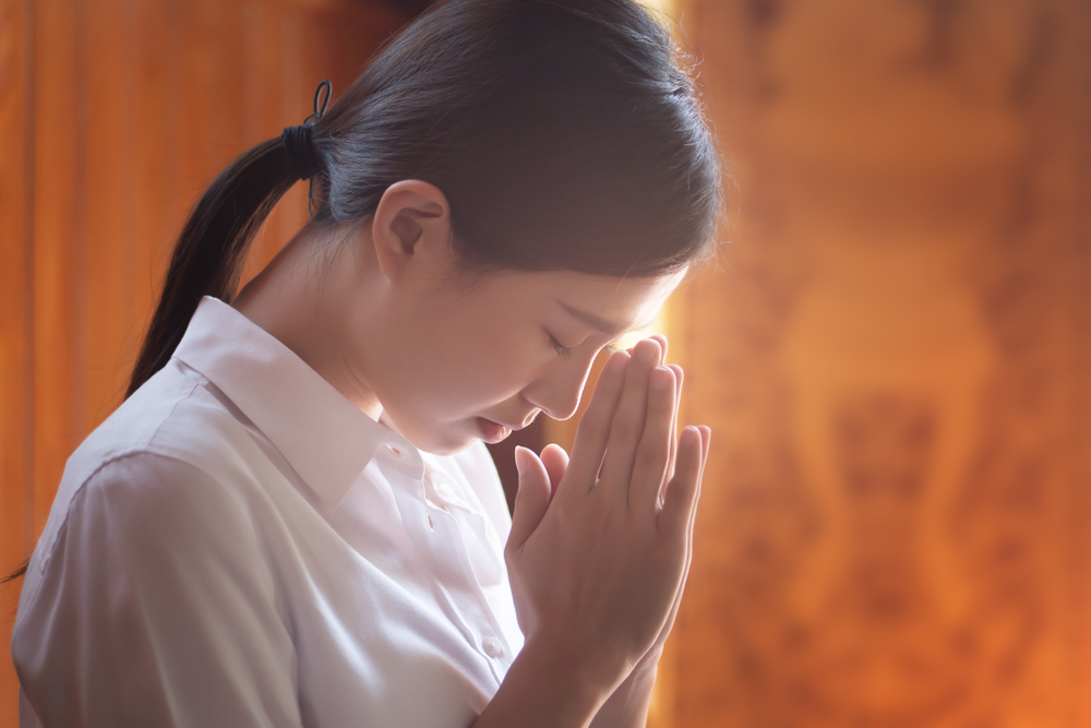 Religious Asian buddhist woman praying. Female buddhist disciple meditating, chanting mantra with prayer hand to the statue of Buddha in temple
