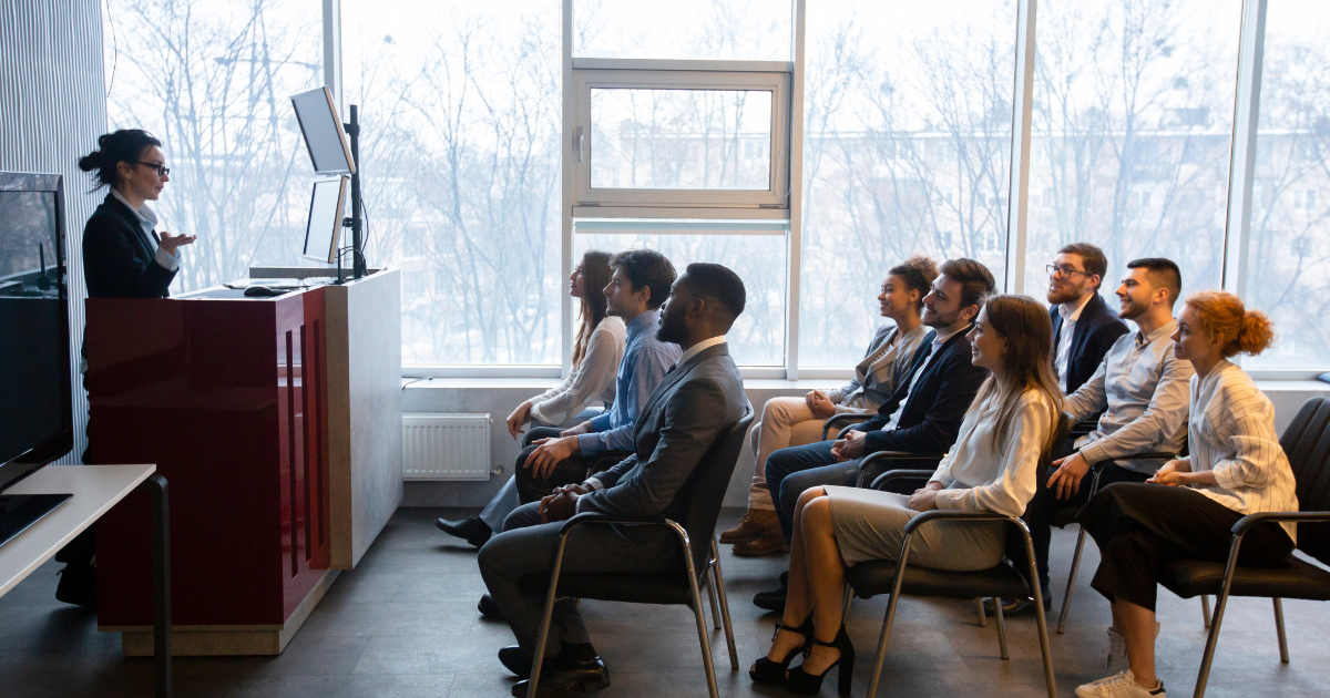A group of people participating in an Enterprise Agile Coaching session, seated in a row with a facilitator taking notes.