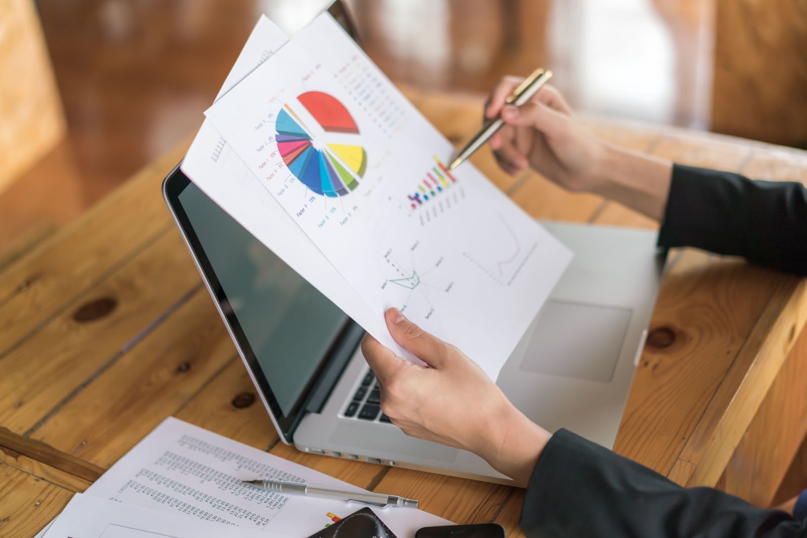 A person analyzing graphs and charts to track the results. Beside the papers, a laptop is also seen