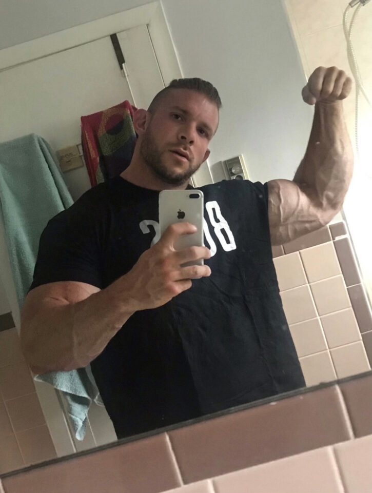 Cody Mac taking an iphone mirror selfie in black and white t-shirt flexing his massive biceps