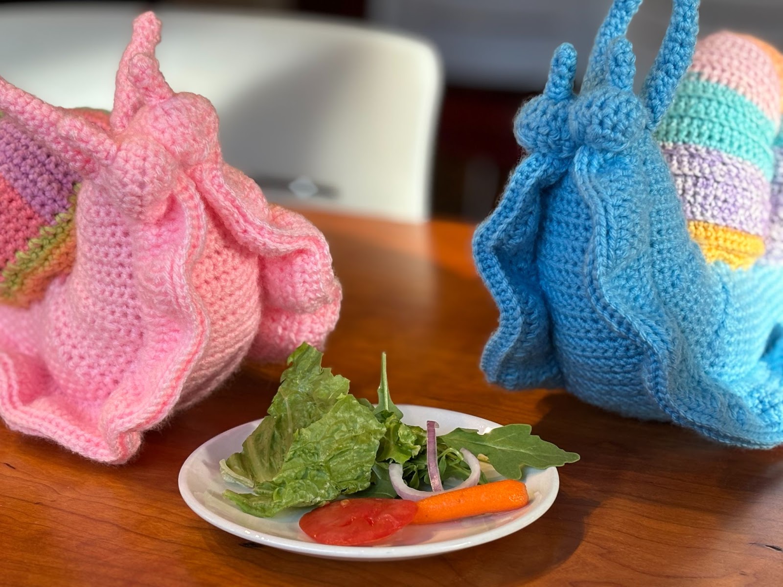 Two crochet snails eating a salad on a wooden table