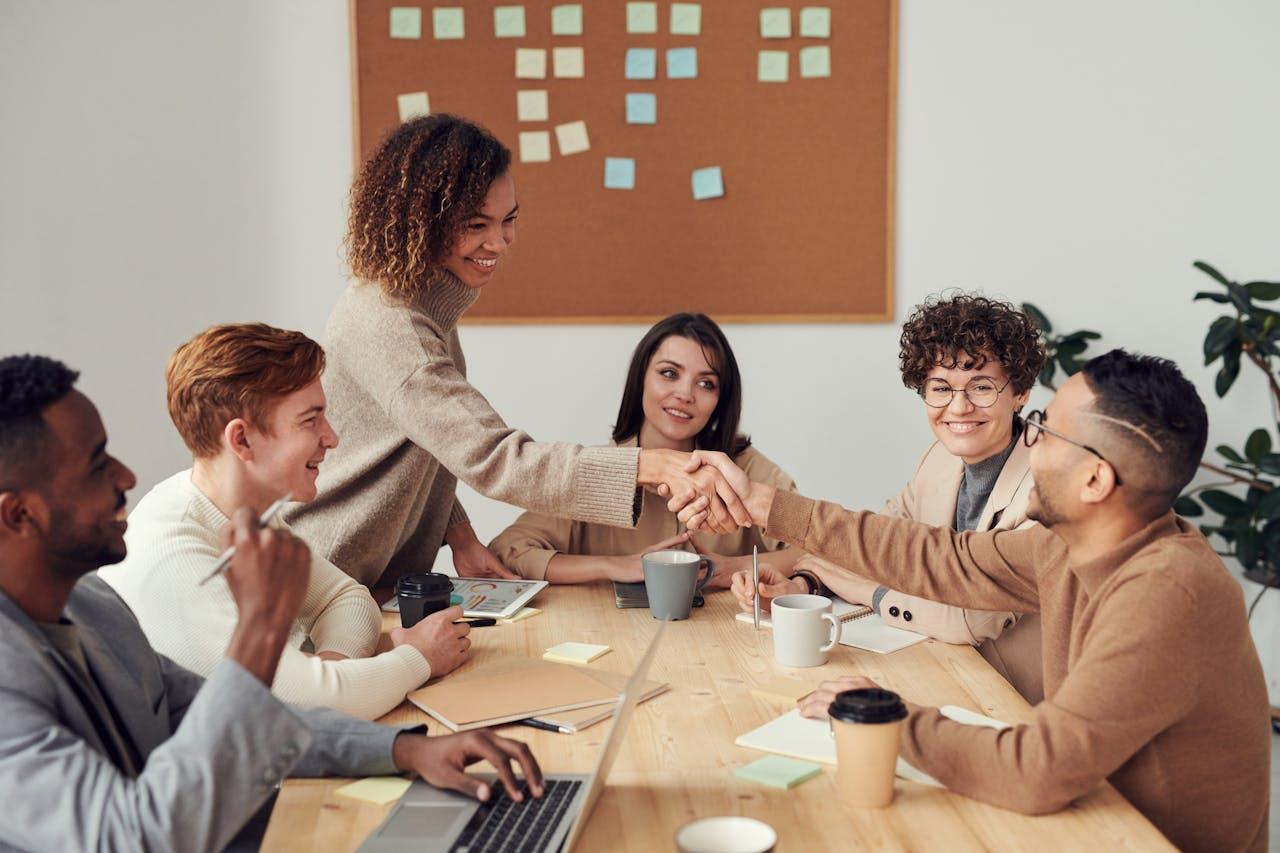 A lady shaking a man’s hand in an office environment while others are smiling