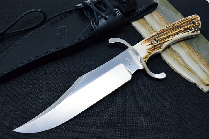 An image featuring the Boker Bowie fixed blade knife on a solid black background. Next to the knife is a leather carrying sheath.