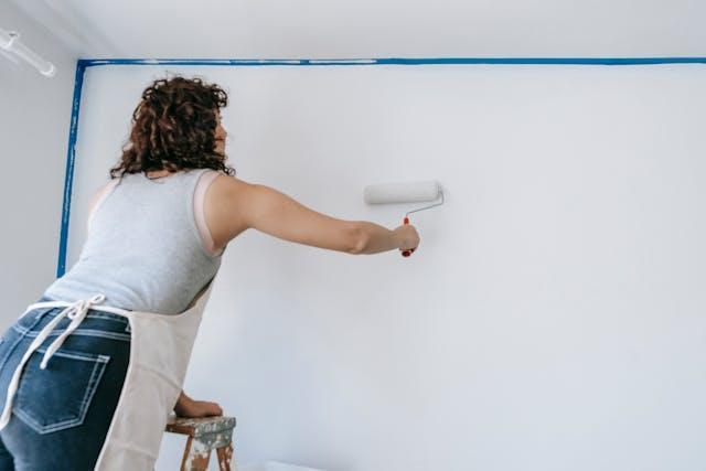  A woman painting a wall in white with a roller