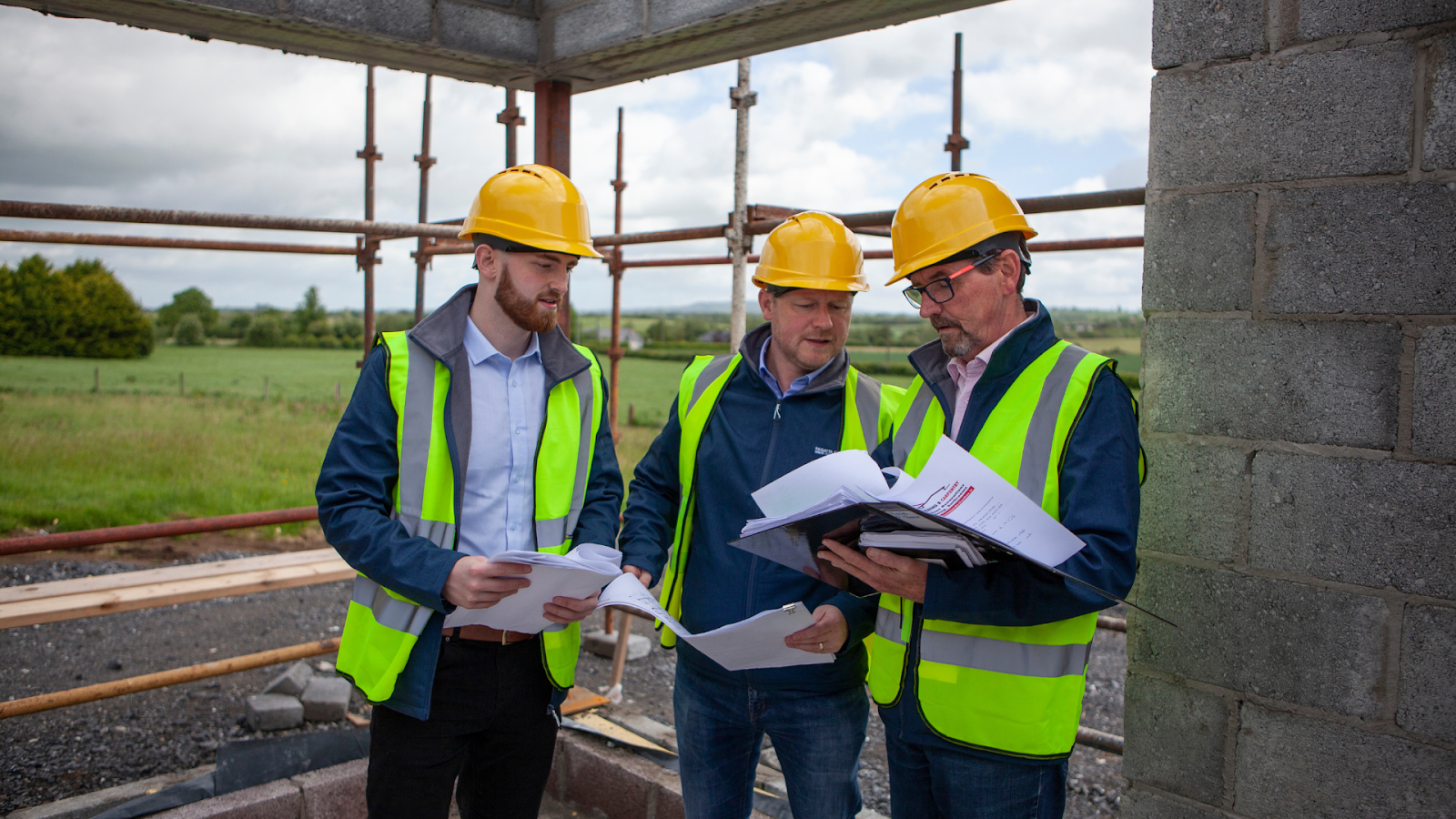 Three men standing on site looking at paperwork. 