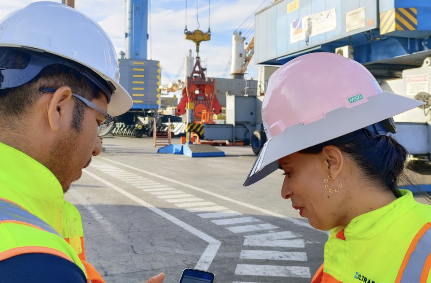 Two people in vests and hard hats looking at a cell phone. 