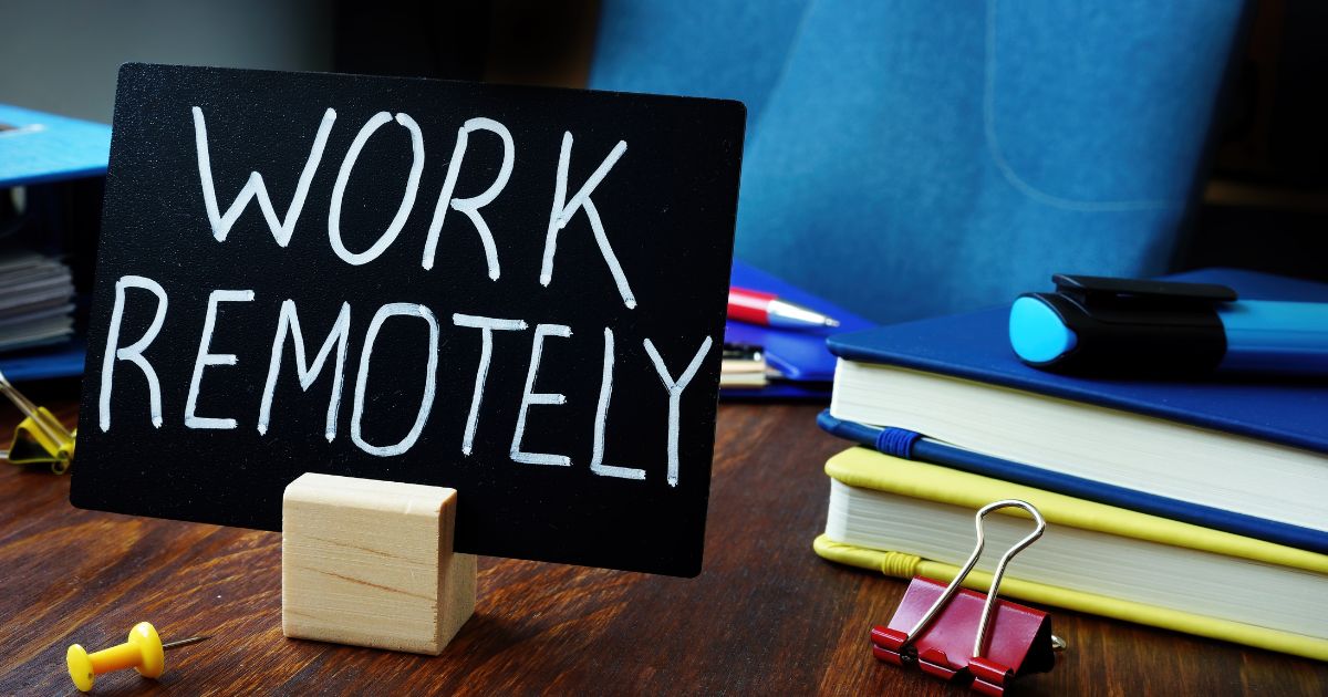 image with a cardboard with "work remotely" written on it and some notebooks beside it