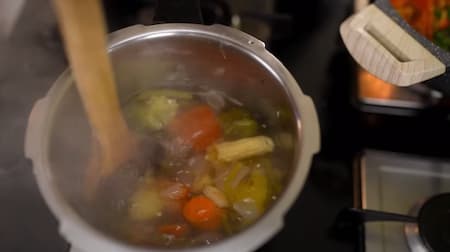 Sliced vegetables in a pressure cooker with water, ready to make stock.