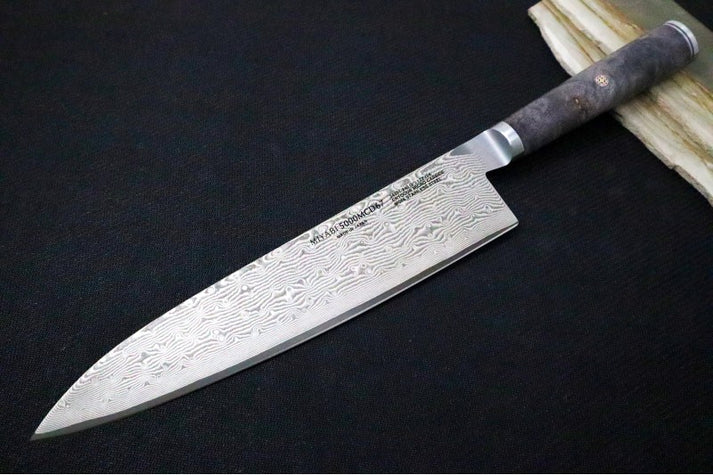 An image showing the Miyabi Black 9.5-inch chef's knife on a solid black and wood background.