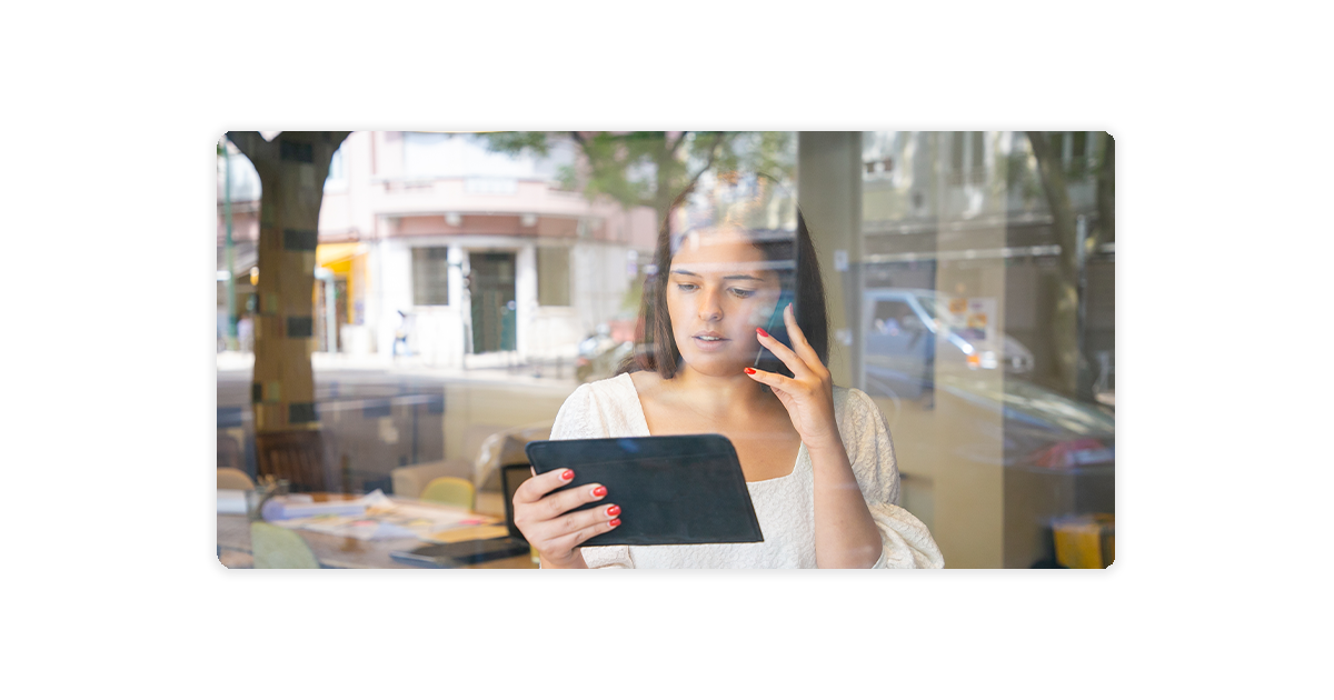 woman in an office using a cell phone to call and tablet to monitor