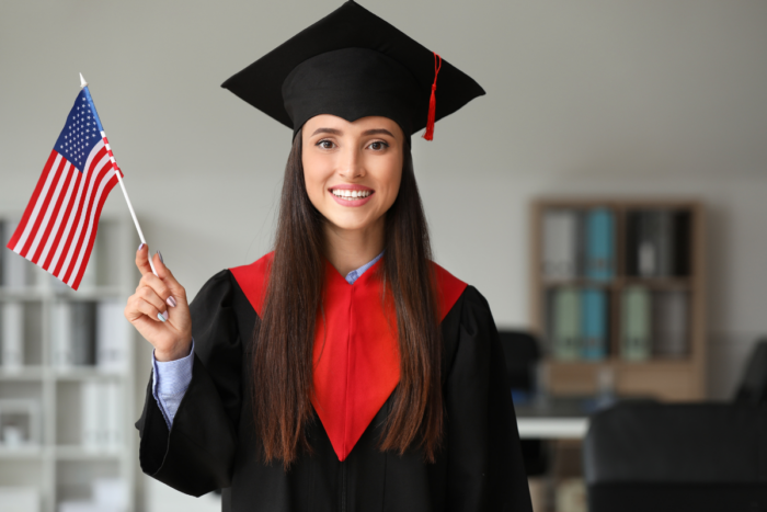 A happy graduate in cap and gown holding an American flag, symbolizing the international opportunities available through management studies at CEFAM.