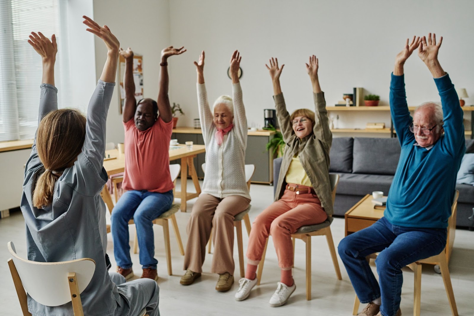 A caretaker leads a group of seniors in a series of chair exercises